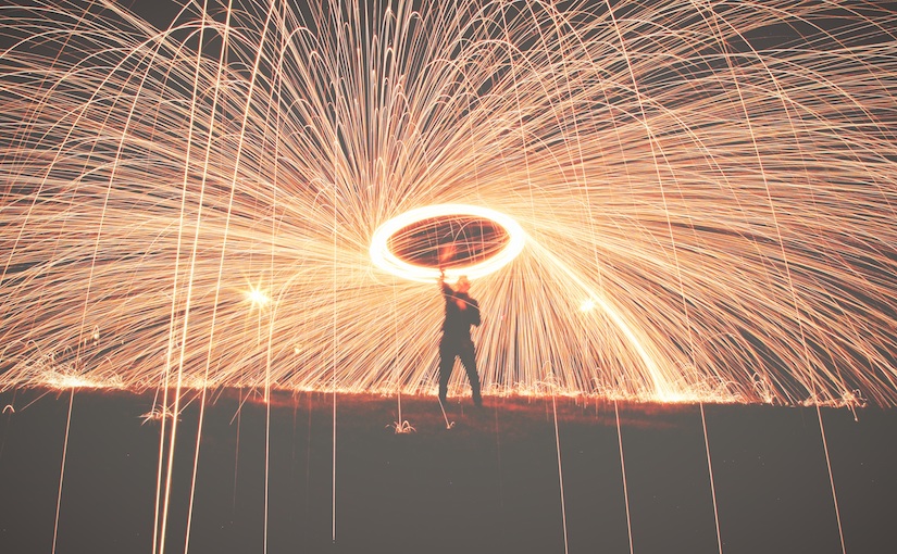 Man holding a spinning sparkler with a long exposure to appear like a network of sparks.