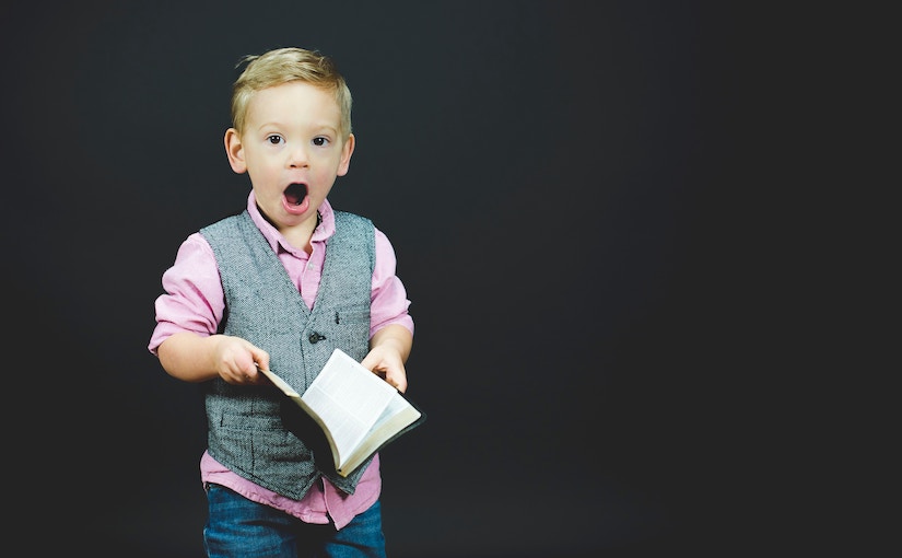 A little boy holding a book with a surprised expression on his face